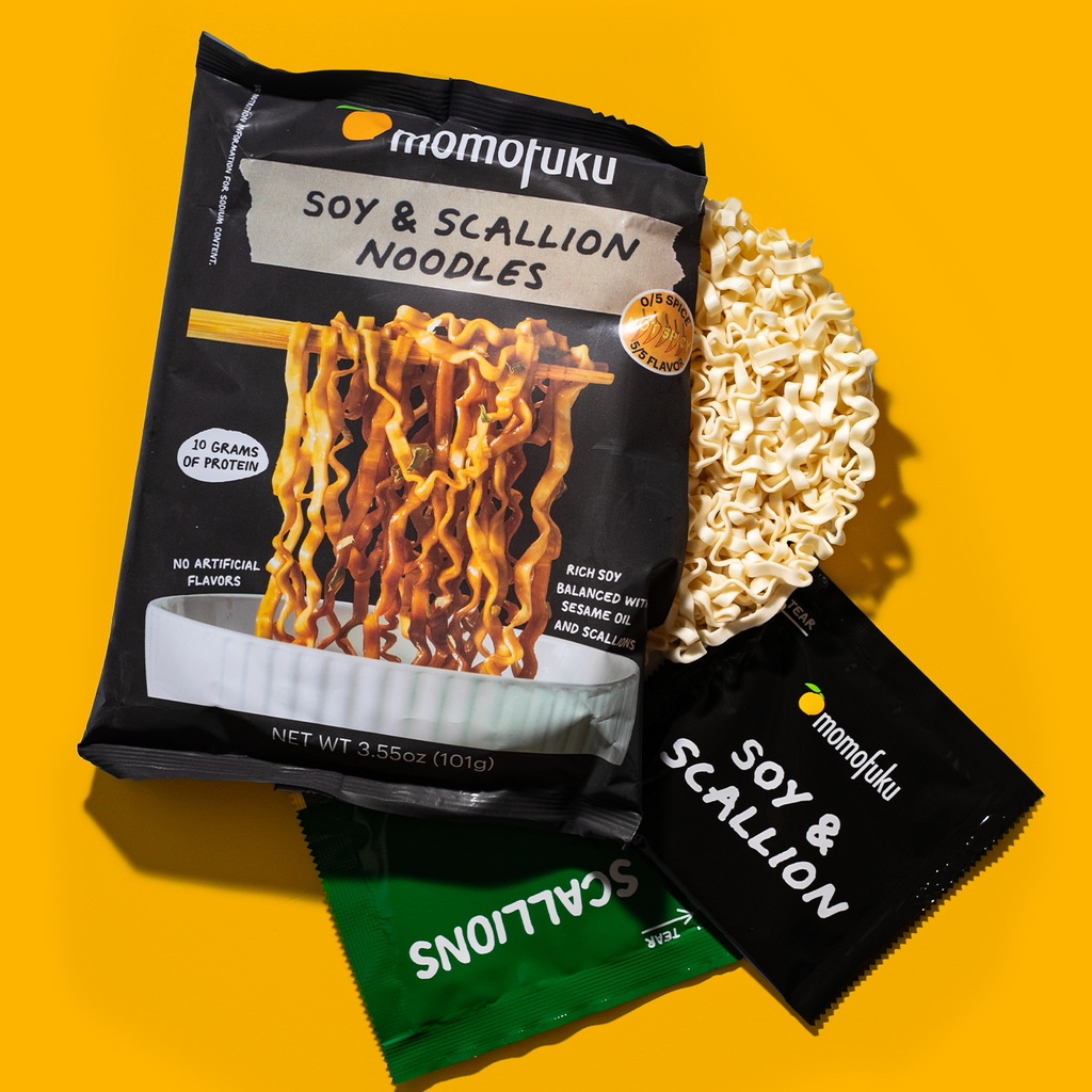 Momofuku Soy & Scallion Noodles package with noodles and seasoning packets on a yellow background